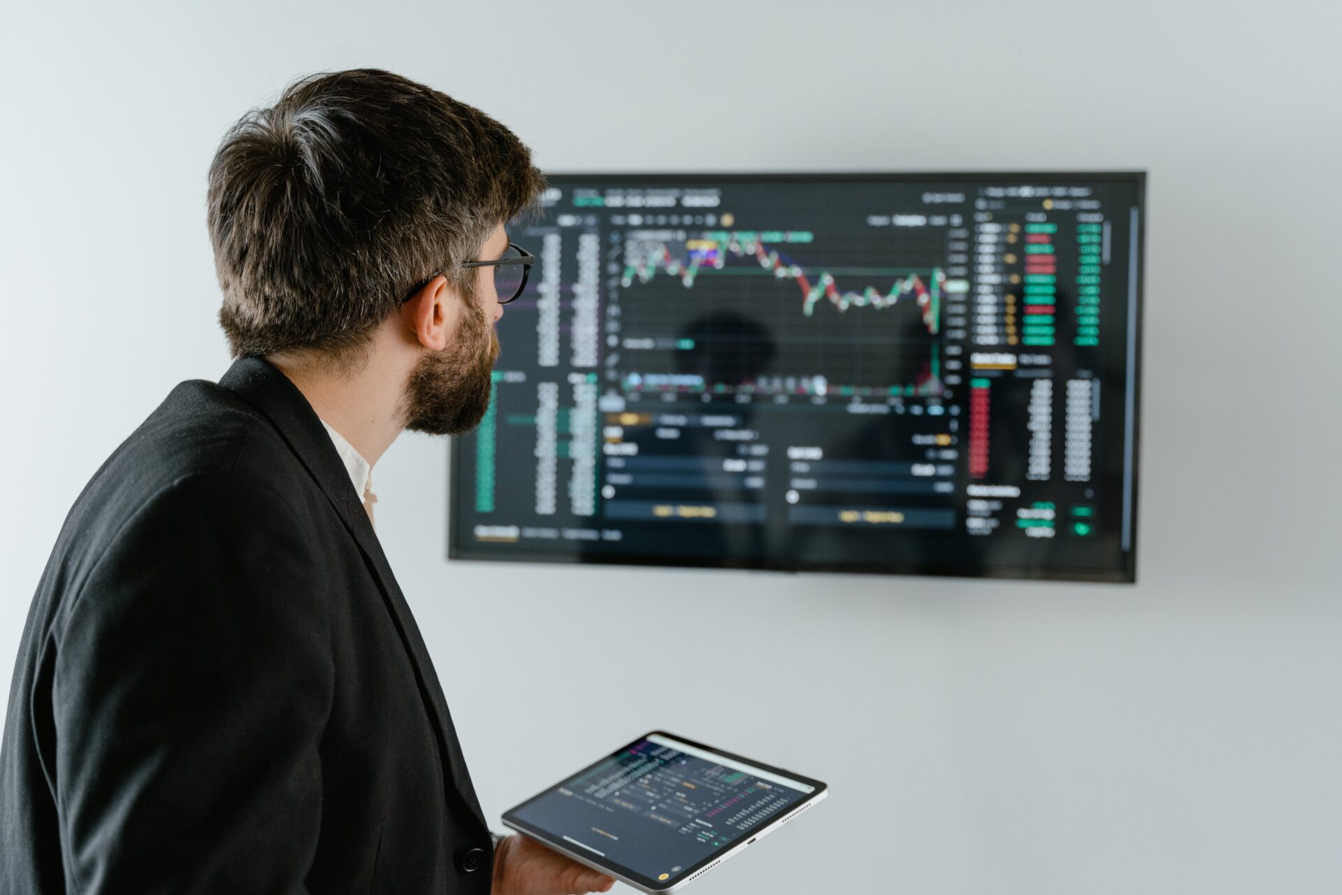 A man holding an ipad in front of a wall with a large screen.